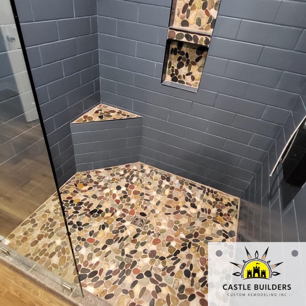 Walk-in shower with dark subway tile, pebble floor, and built-in niche